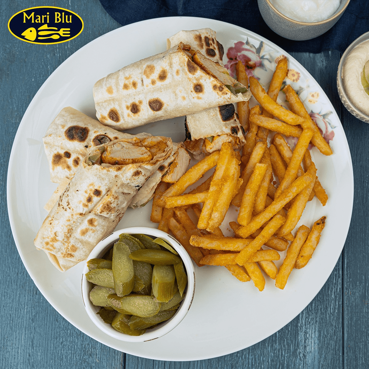 Mari Blu chicken wrap with crispy fries and a side of pickled cucumbers.
